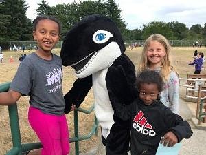 三名学生站在学校吉祥物虎鲸旁边
