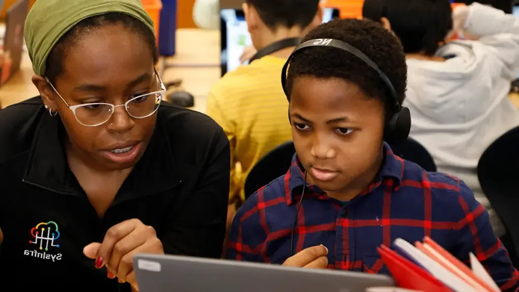 Elementary school student sits with volunteer during week of code to complete coding activity